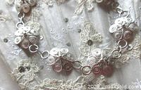 Close-up showing filigree flower details and the spring clasp, highlighting the delicate craftsmanship and silver finish.