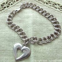Photo shows a vintage sterling silver bracelet with linked chain and a heart-shaped charm. Clasp is a lobster style and marked '925'. Bracelet is laid flat on fabric surface.