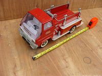 Vintage Tonka metal fire engine truck with tape showing approx. 17 inches length on wood background.
