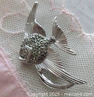 Close-up front view of the vintage fish brooch showing marcasite stone details and rhodium plated fins and tail on a pink lace background.