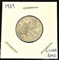 Front side of 1939 Canadian 25 cent silver coin showing a caribou in the center, held in a white cardboard holder stamped with '1939' and 'silver 8000'.