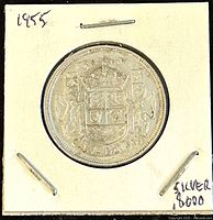 Image showing the reverse side of the 1955 Canadian 50 cents silver coin inside a cardboard holder, displaying the Canadian coat of arms and the denomination.