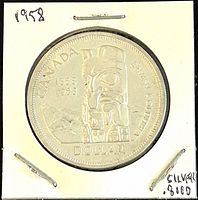 Front of the 1958 Canadian Silver 1 Dollar Coin showing the totem pole and Canadian centennial text.