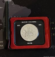 Front view of the 1971 British Columbia silver dollar coin mounted in black plastic holder surrounded by red velvet inside a display case.