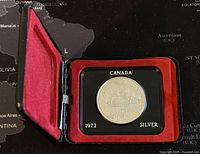 1972 Canadian silver dollar displayed in black case with red velvet interior, showing front of case open and coin visible.