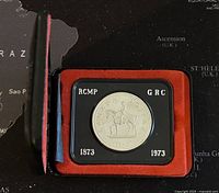 Image showing the silver coin in black and red display case with mounted RCMP officer and dates 1873-1973