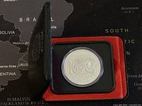 Top angle view of coin inside black display case with red velvet lining on a map background.