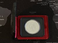 Front of the coin in its red velvet-lined protective display case showing the design with a cowboy on a bucking horse.