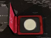 Silver coin with Parliament Buildings and date on reverse in hard plastic case inside red velvet-lined display case.