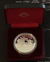 Front view of the coin in a red velvet lined hinged display case with maple leaf emblem on the inside lid, showing the train design on the coin reverse.