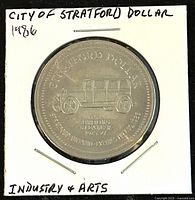 Front side of the 1986 City of Stratford trade dollar coin with automobile image and inscription.