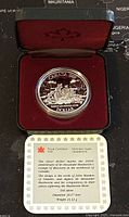 Coin displayed in red velvet-lined protective case along with the Royal Canadian Mint certificate card describing the coin's historical significance, dimensions and silver content.