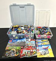 Full view of two plastic boxes filled with assorted LEGO bricks and several instruction manuals laid out in front.