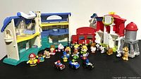 Wide view of all Fisher Price Little People figures, vehicles, and playsets including house, barn, water tower on black surface.