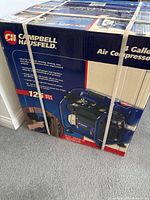 Strapped unopened box of Campbell Hausfeld air compressor showing front and side with product image and branding.
