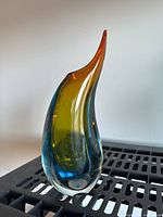 Front view of the multicolored art glass vase, showing curved teardrop shape with orange, yellow, green, and blue hues