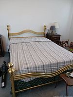 Full view of brass bed frame made up with striped bedspread, showing headboard and footboard with brass finials.