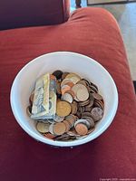 A white bowl filled with various Canadian coins and a folded Canadian $5 bill.