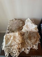 Overview of multiple folded crochet and lace doilies in assorted cream, beige, and white coloring on a wooden table