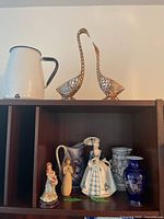 Shelf with white enamel pitcher, metal bird sculptures, two small figurines, and multiple blue and white ceramic vases and pitchers.