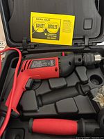 Jobmate impact drill in carrying case with red and black body and safety goggle warning card visible