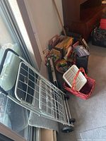 Photo showing foldable bundle buggy with metal frame and 2 wheels in front of a pile of office supplies including the letter organizer and other items on the floor.