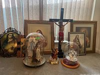 Lot overview showing four framed prints behind wooden crucifix, two glass domes with statue and lamp, and metal crown statue