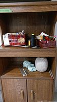 Wooden shelf with assorted sewing supplies including spools of thread, scissors, and thread cones.