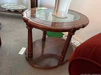 Photo showing one wooden side table with round scalloped edge top, inset glass with etched motif and lower shelf.