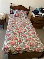 Twin bed setup with floral pattern mattress cover, wood headboard and footboard with rounded finials, visible side rails on floor.