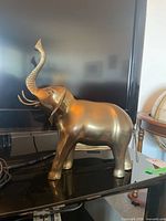 Front side view of vintage brass elephant statue placed near a TV screen.