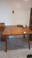 Square wooden dining room table with rounded corners and four turned legs, shown without leaf attached.