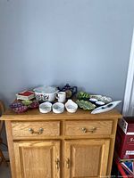 Wide view of all 18 ceramic serving and decorative pieces arranged on a wood cabinet, showing variety and condition