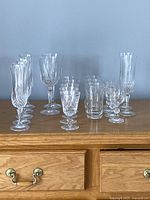 Wide shot of all 21 pieces of stemware arranged on a wooden surface, showing tall champagne flutes, wine glasses, water goblets, tumblers, liqueur glasses, and glass champagne flutes.