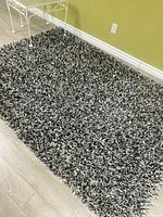 Full view of the black and white shaggy rug on a light hardwood floor with pale yellow wall background.