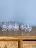 Two sets of vintage low ball glasses displayed on a wooden surface against a plain background, showing six heavy crystal glasses on the left and five cut glass glasses on the right.