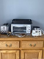 Photo showing the full lot on wooden dresser with toaster, toaster oven, mixers, baking dishes.