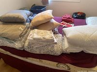 Lot of bedding items on a bed: pillows, sheets, bedding sets, blankets in various neutral colors.