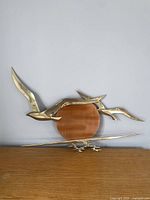 Front view of the brass seagull wall decor with a copper sun background on a plain wall above a wooden surface.