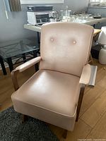 Front angled view of pink pearlized pleather rocking chair showing padded seat, back with button tufting, and wooden armrests/base