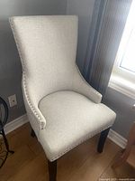Front and side views of the light gray living room chair placed near a window and curtain, showing the nailhead trim and shape.