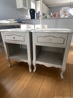Front view of two white wood vintage bedside tables side by side, showing drawer and open shelf