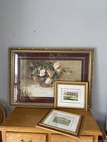 Set of three framed prints shown on wooden surface - one large floral print and two smaller Walter Campbell golf prints