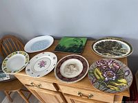 Full view of all seven vintage decorative plates arranged on wooden cabinet showing various designs