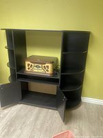 Front view of tall black entertainment unit with curved side shelves, a wooden record player on central shelf, and open cabinet with doors below.