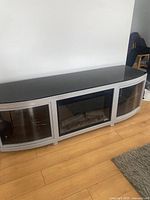 TV stand with integrated electric fireplace insert shown from front, placed against a wall on wooden floor.