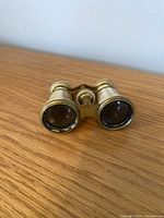 Front view of vintage mother of pearl opera glasses showing lenses and brass framing on wooden surface.