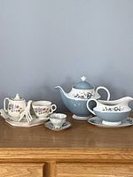 Photo showing Royal Doulton Rose Elegans teapot, gravy boat with plate, and small china set including sugar pot and creamer on wood surface.