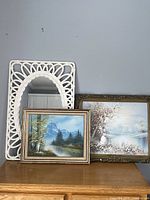 Vintage white resin strocco mirror with woven pattern frame, two framed landscape paintings behind it