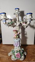 Full frontal view of a porcelain 5-arm candelabra with a hand-painted female figure and floral detailing, white background, showing size and design.